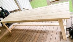 a dog sitting under a wooden table on a deck next to a bbq grill