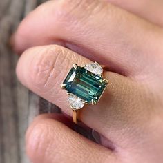 a woman's hand holding a ring with an emerald and two diamonds on it