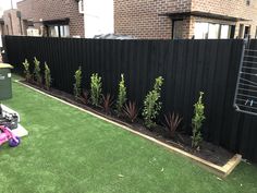 a black fence is next to some plants and a pink lawn mower in front of it