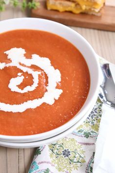 a bowl of tomato soup on a wooden table with a spoon and napkin next to it