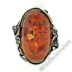 "This stunning vintage cocktail ring was hand crafted from solid sterling silver and features an oval cabochon amber stone neatly set at the center. The amber shows unique natural inclusions and displays a gorgeous translucent orange color throughout with an absolutely rich look. The ring features lovely leaf designs along with wire work that elegantly frames the stone and swirls with open work at the sides of the shank. This fancy handmade setting along with the large size on this lovely amber, Oval Amber Cabochon Jewelry, Antique Oval Collectible Rings, Hallmarked Amber Oval Cabochon Jewelry, Vintage Oval Cabochon For Jewelry Making, Ornate Oval Cabochon Jewelry, Heirloom Oval Amber Jewelry, Heirloom Amber Oval Jewelry, Antique Sterling Silver Oval Cabochon Jewelry, Antique Sterling Silver Cabochon Rings