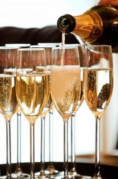 champagne being poured into wine glasses in front of another glass filled with white and gold liquid