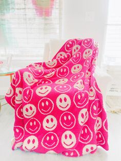 a pink and white blanket with smiley faces on it in front of a window,