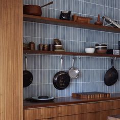 pots and pans are hanging on the wall in this kitchen with blue tile backsplash