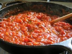 a skillet filled with tomato sauce on top of a stove next to a wooden spoon