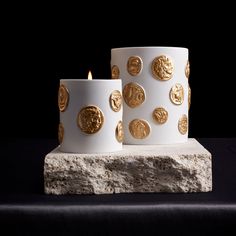 two white candles with gold coins on them sitting on a rock next to each other