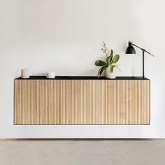 a white wall with a wooden cabinet and lamp next to it on top of a table