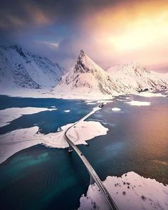 an aerial view of a road in the middle of snow - covered mountains and water