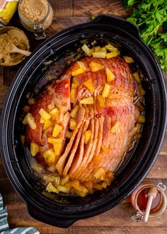 a slow cooked ham in a crock pot on a wooden table next to spices and seasonings