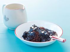 a white bowl filled with chocolate cake next to a mug on top of a blue table