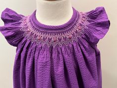 This is a finished, smocked dress, size 18 months, in solid purple seersucker. It has angel sleeves hemmed plain, and three buttons with elastic button loop at the back. The dress has a 4" hem. It is smocked with DMC cotton floss. Purple Smocked Dress For Spring, Spring Purple Smocked Dress, Cotton Smocked Dress With Flutter Sleeves, Purple Smocked Summer Dress With Ruffles, Dress Pattern Free, English Smocking, Smocked Bishop Dress, Angel Sleeves, Hand Smock