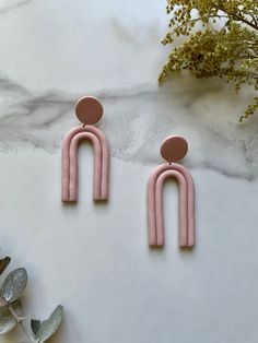 two pink earrings with circular shapes on top of a marble table next to flowers and leaves