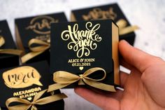 a hand holding a small black box with gold foil lettering and ribbon around the edges