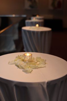 a white table topped with a candle and some flowers on top of the tablecloth