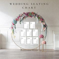 the wedding seating chart is displayed on a round metal stand with flowers and greenery