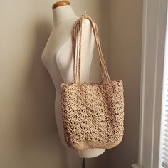 a white mannequin holding a beige crocheted bag on it's shoulder