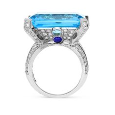 Bold and feminine, this gemstone ring defines a beautiful design showcasing an emerald cut blue topaz center stone in a diamond adrorned setting. On either side of the center gemstone lay two smaller round blue topaz and a cabochon cut blue sapphire for extra detailing. The ring flows into an embellished shank to enhance an eye catching appeal. Polished to a bright shine, this look packs a big visual punch. 
24.80 carat Emerald cut Blue topaz
0.60 carat cabochon round cut Sap Blue Diamond Ring With Diamond Accents Emerald Cut, Blue Emerald Cut Diamond Ring With Accents, Blue Emerald Cut Diamond Ring With Diamond Accents, Luxury Sapphire Ring With Emerald Cut And Gemstone Accents, Luxury Emerald Cut Sapphire Ring With Gemstone Accents, Luxury Emerald-cut Sapphire Ring With Gemstone Accents, Blue Radiant-cut Emerald Ring In Fine Jewelry Style, Blue Radiant Cut Emerald Ring In Fine Jewelry, Blue Radiant-cut Emerald Ring Fine Jewelry