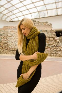 a woman wearing a green knitted scarf and black leggings standing in front of a stone wall