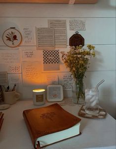 a table topped with a book and vase filled with flowers next to a candle on top of a white counter