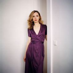 a woman in a purple dress leaning against a wall