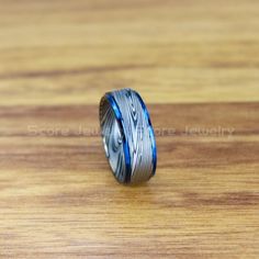 a wedding band with blue and silver inlays sits on a wooden surface,