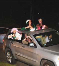 four people in the back of a silver jeep at night with their hands up and smiling