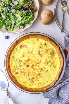 an overhead view of a quiche next to a bowl of salad and utensils