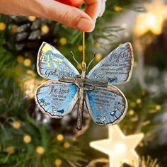 a hand holding a blue butterfly ornament in front of a christmas tree with lights