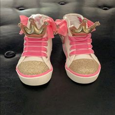 a pair of pink and gold high top sneakers with crowns on the side, sitting on a black surface