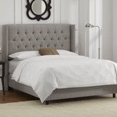 a bed with white linens and a gray headboard in a bedroom next to a window