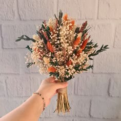 a hand holding a bouquet of flowers in front of a brick wall