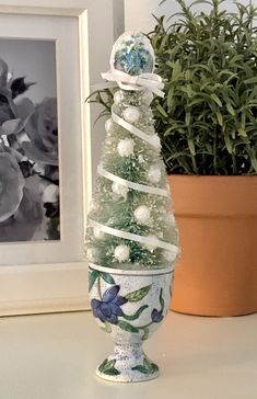 a glass christmas tree sitting on top of a table next to a potted plant