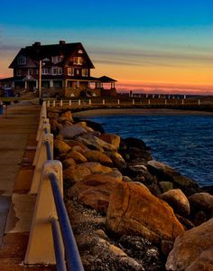 a house sitting on the side of a body of water next to a rocky shore