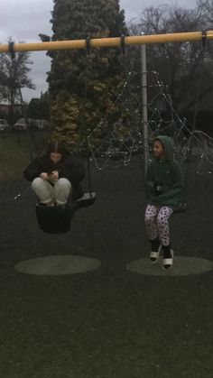 two people sitting on swings in the park