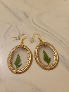 "These framed pressed flower earrings are handmade and use crystal clear hot glue to allow the flower to be seen inside the frame. The earring hooks are hypoallergenic, gold-plated stainless steel and come with a rubber back. The framed pressed flowers measure 1.25\"x1\" for the oval frame and 1\"x0.75\" for the rectangular frame. The flower color and frame shape can be customized." Gold Botanical Earrings With Pressed Flowers, Botanical Gold Earrings With Pressed Flowers, Gold Resin Earrings With Birth Flower Detail, Gold Resin Earrings With Birth Flower, Handmade Gold Botanical Earrings, Nature-inspired Gold Earrings With Pressed Flowers, Nature-inspired Gold Flower Earrings With Pressed Flowers, Botanical Style Gold Resin Jewelry, Botanical Gold Earrings With Birth Flower