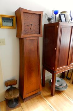 a tall wooden grandfather clock sitting next to a chair and cabinet in a living room