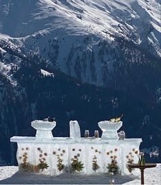 an ice sculpture on top of a snow covered slope with mountains in the background,