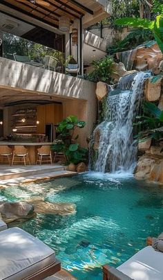 an outdoor pool with waterfall and lounge chairs next to it in front of a house