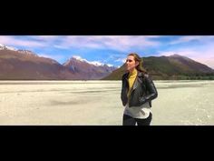 a woman standing in the middle of a desert with mountains in the backgroud