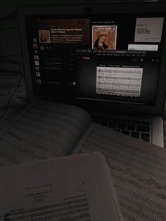 an open book sitting on top of a laptop computer next to music sheets and sheet music