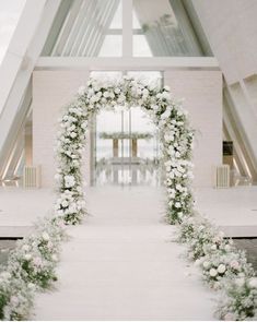 an arch with flowers and greenery is in the middle of a wedding ceremony aisle