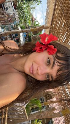 a beautiful young woman laying on top of a wooden chair next to a table with a red flower in it's hair