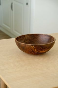 a wooden bowl sitting on top of a table next to a white cabinet and counter