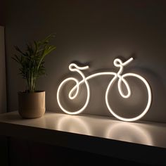 a bicycle is lit up on the wall next to a potted plant