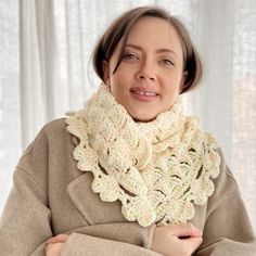 a woman wearing a white crochet scarf with her arms crossed and looking off to the side