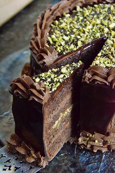 a chocolate cake with pistachios on top is cut in half and ready to be eaten