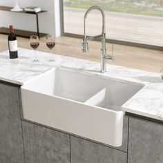 a white sink sitting under a kitchen faucet next to a wine glass and bottle