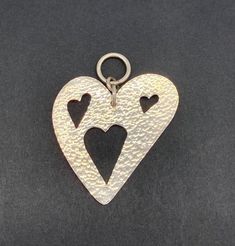 a heart shaped pendant with two hearts cut out of it's sides on a black surface