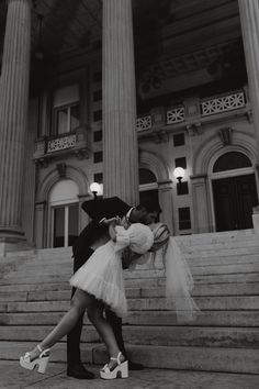 a man and woman kissing on the steps of a building with columns in the background