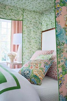 a bedroom with green and pink wallpaper, white bedding, and floral pillows